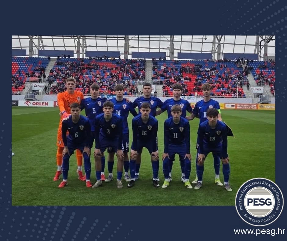 Youth soccer team in blue uniforms posing for a group photo on a green field, with a goalie in orange at the back left.