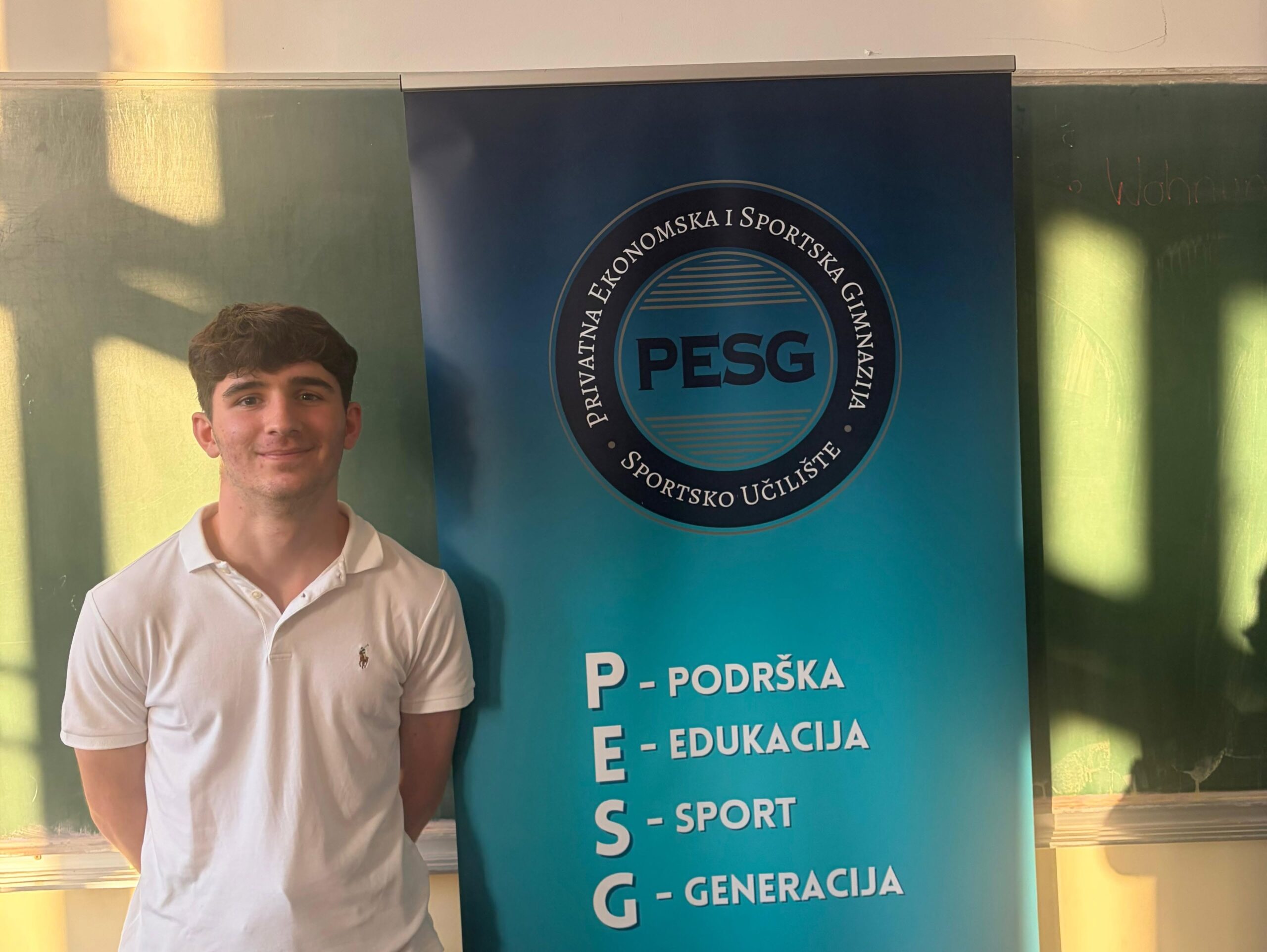 Smiling young man in a white polo shirt standing beside a blue banner featuring a circular PESG logo and educational program text.
