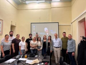Group of about a dozen adults posing in a classroom/meeting room with a projector screen in the background showing a cartoon and a thank-you message.