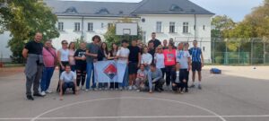 Group of students and adults posing on an outdoor school basketball court with a white building behind them.